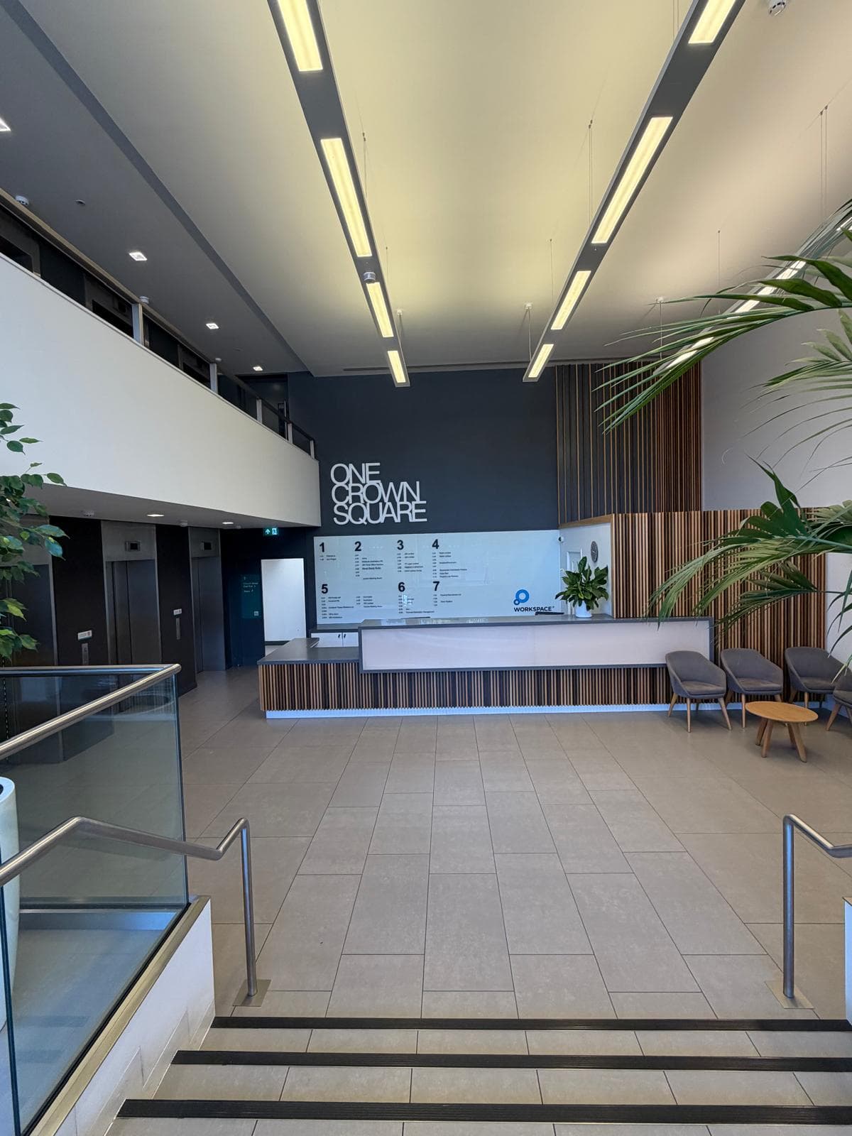 The stone stair down to reception under the atrium, with the desk, planting and waiting chairs at the bottom
