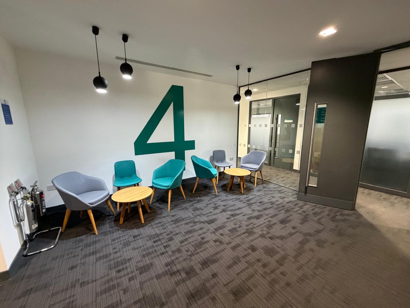 Fourth floor breakout area with teal and grey tub chairs, round timber tables, black pendant lights and a large painted number four on the wall
