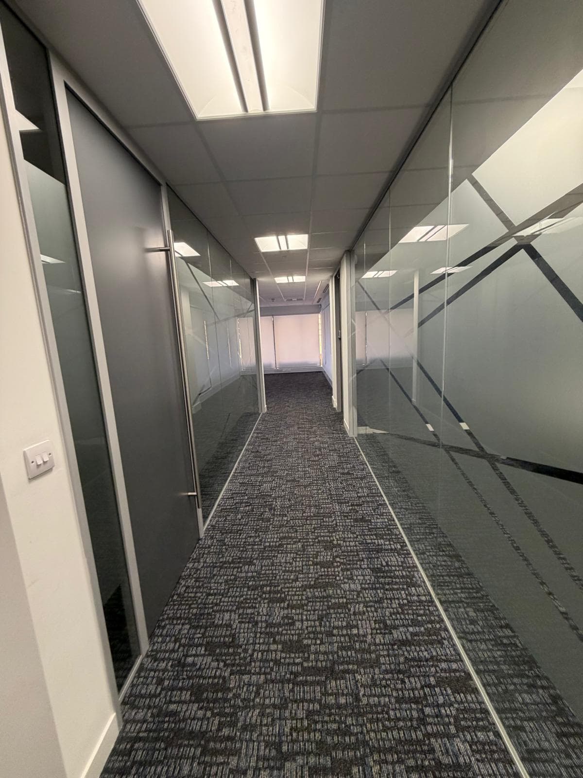 A corridor running between full-height glazed partitions with frosted manifestation