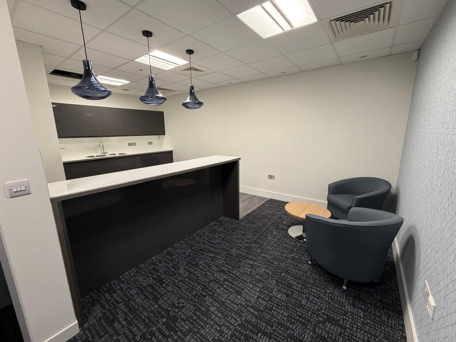 A floor tea point with dark units, a white peninsula counter, pendant lights and two armchairs