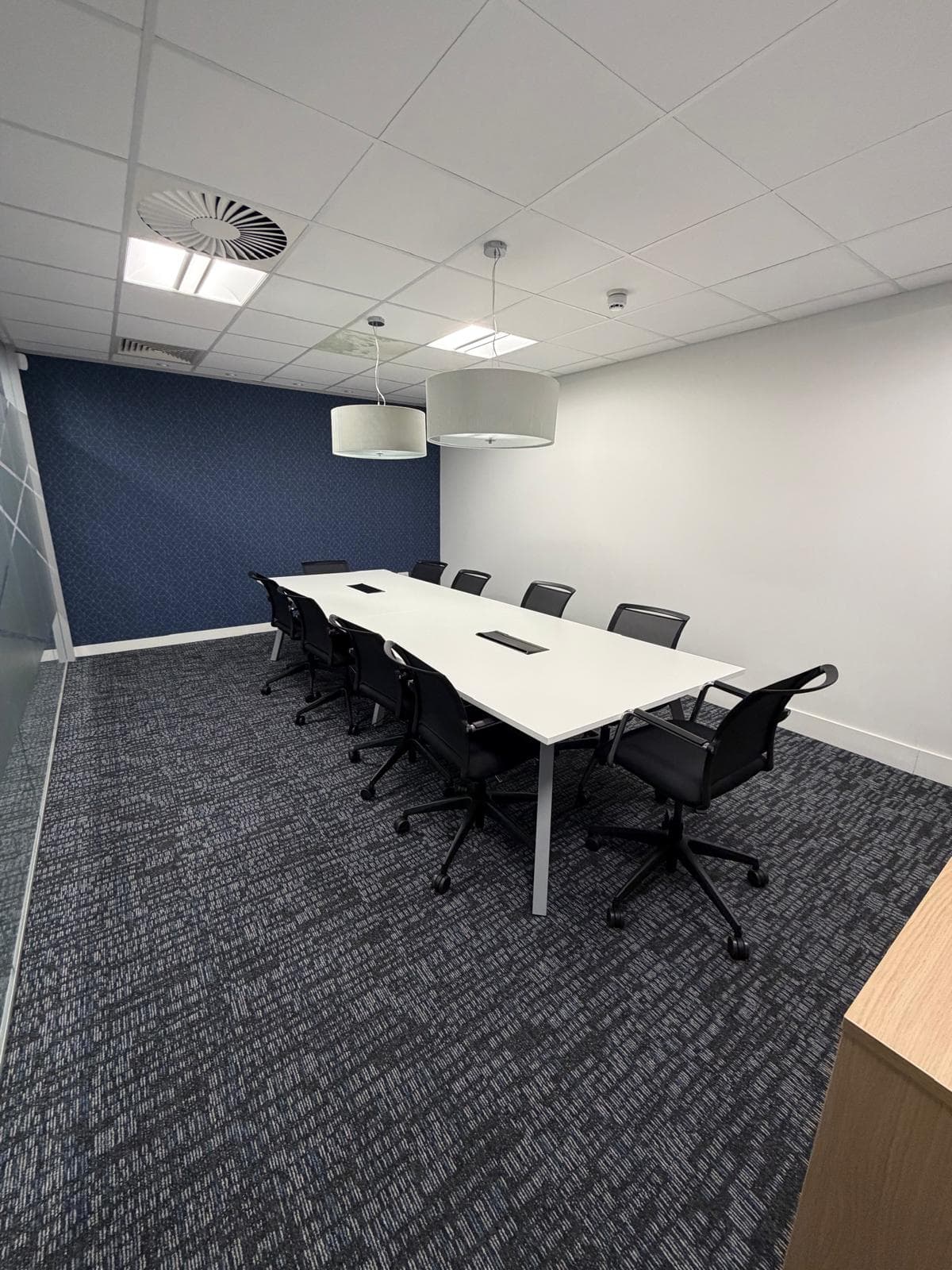A boardroom with a long white table, black chairs, drum pendant lights and a deep navy feature wall