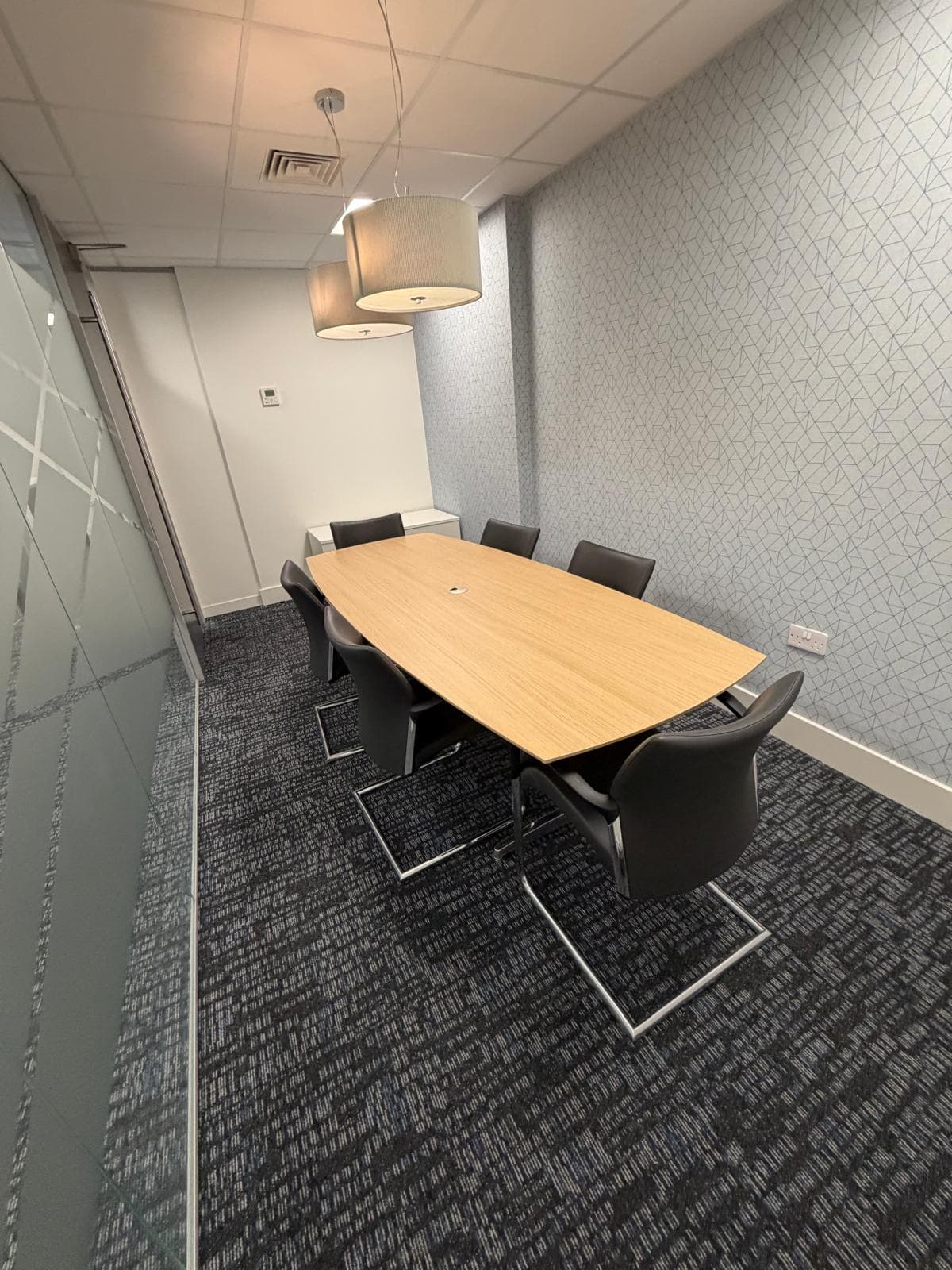 A meeting room with a boat-shaped oak table, six black cantilever chairs and a drum pendant light