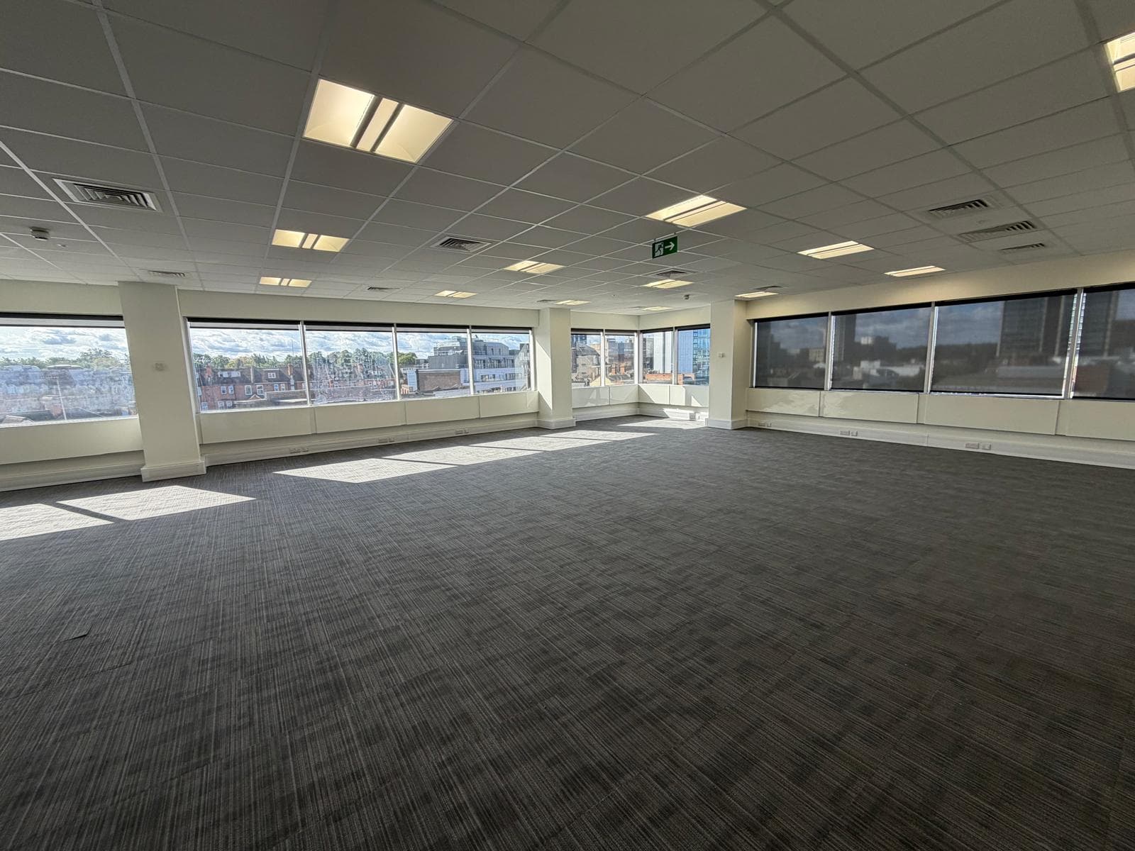 An empty suite with new carpet and windows on two sides looking over the rooftops of Woking