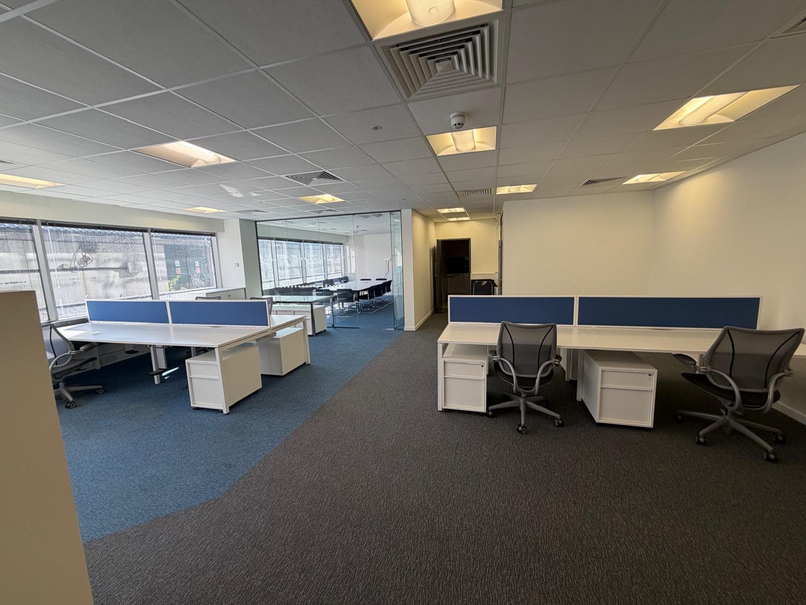 A fitted floor with bench desking, blue desk screens, task chairs and pedestals, lit by windows along one side