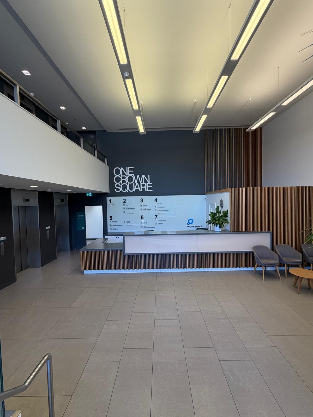 The full-height reception hall, with linear ceiling lights, lift doors to the left and the reception desk against the charcoal signage wall