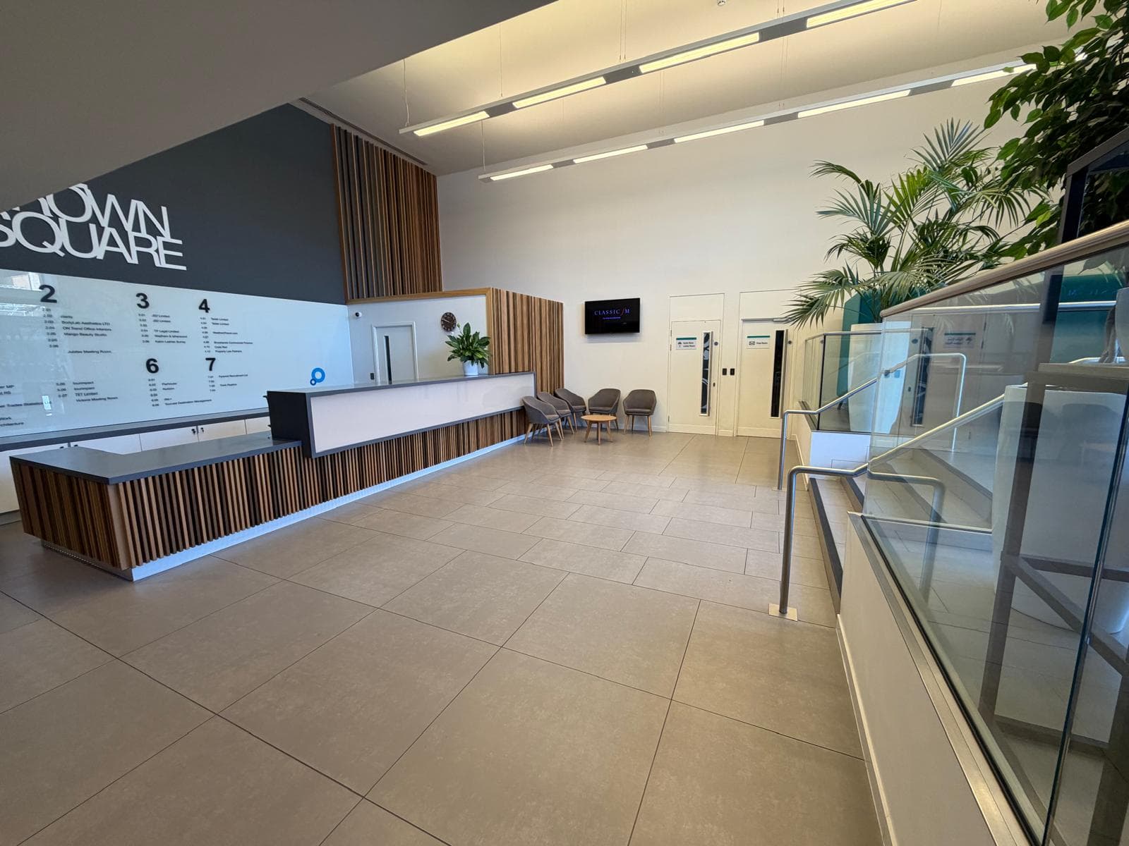 The One Crown Square name in white letters on a charcoal wall above the tenant directory, with the timber-fronted reception desk running along beneath it