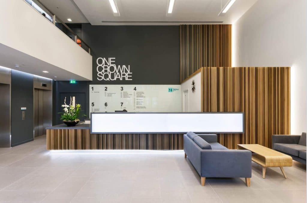 The double-height reception at One Crown Square, with the building's name in white letters on a charcoal wall and full-height timber slat cladding